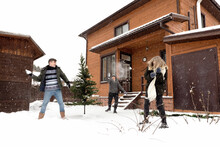 Man, Young Woman And Adult Woman Playing Snowballs Near Wooden House