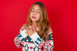 © Jihan - little kid girl wearing knitted sweater christmas over red background expresses happines, laughs pleasantly, keeps hands on heart