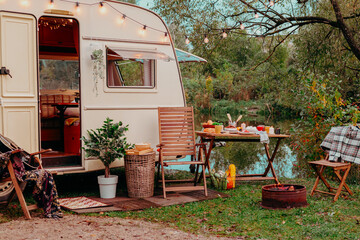 Wall Mural - trailer of mobile home or recreational vehicle stands on shore of pond in camping in autumn near table set, concept of family local travel in native country on caravan or camper van and camping life