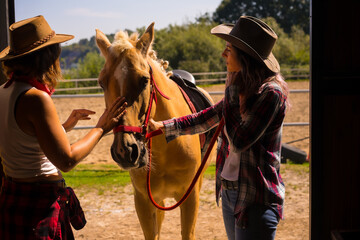 Two cowgirl women entering the stable with a horse on a horse, with South American outfits