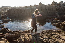 Teenage Girl Walking Across Jagged Rocks, Exploring Rock Pools By The Ocean