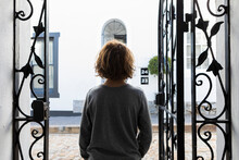 A Boy Standing Looking Out Of Open Ironwork Gates. 