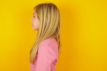 Wall Mural - Profile portrait of nice caucasian little kid girl wearing long sleeve shirt over yellow background look empty space toothy smile