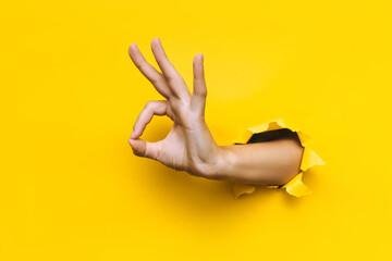 the woman's hand shows with a gesture that everything is fine (ok). torn hole in yellow paper. the c