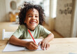 © JenkoAtaman - Smiling african american child school boy doing homework while sitting at desk at home