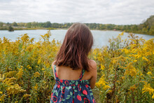 Rear-view Of Small Child Standing In Prairie Of Wildflowers By Lake