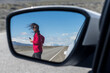 © Cavan Images - Woman crossing the route seen through side-view mirror of car