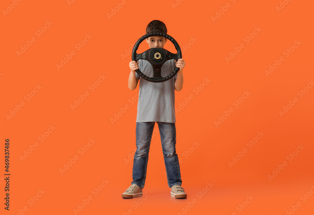 Little boy with steering wheel on color background