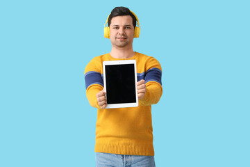 Wall Mural - Young man with tablet computer and headphones on color background