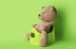 Cute toy bear sitting on potty on green background