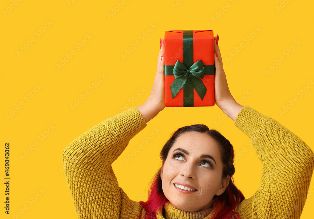 Beautiful woman with Christmas gift box on yellow background