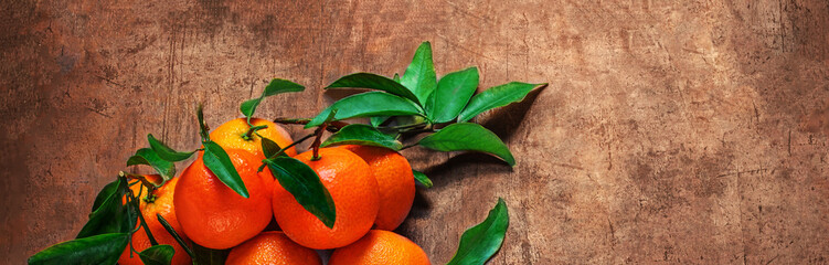 Wall Mural - Mandarines oranges fruits or tangerines with green leaves on a dark wooden background. Copyspace.