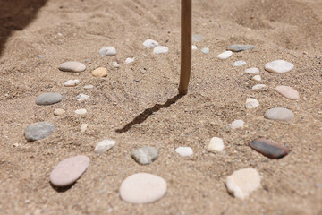 Wooden stick and pebbles on sand showing time by shadow