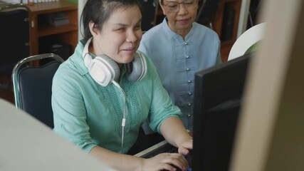 Wall Mural - Authentic blind person woman with headphone using computer with braille display assistive device discussing with senior colleague woman in workplace, handheld shot.