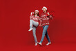 Full body young couple friends two man woman 20s in sweater hat hold gift bag do winner gesture isolated on plain red background studio. Happy New Year 2022 celebration merry ho x-mas holiday concept.
