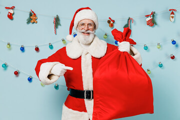 Wall Mural - Old Santa Claus man wears Christmas hat red suit clothes carrying hold point on bag with gifts isolated on plain blue background studio. Happy New Year 2022 celebration merry ho x-mas holiday concept.