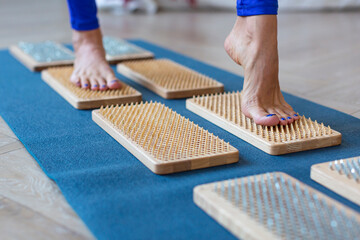 Female feet stand on a board with sharp nails over white background. Sadhu's board - practice yoga. Pain, trials, health, relaxation, cognition.