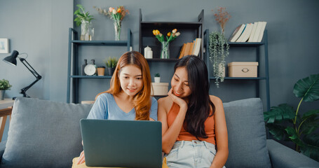 Wall Mural - Two Asia lesbian women site on couch together looking at laptop screen in living room at home together. Happy couple roommate ladies enjoy web surfing online shopping, Lifestyle woman at home concept.