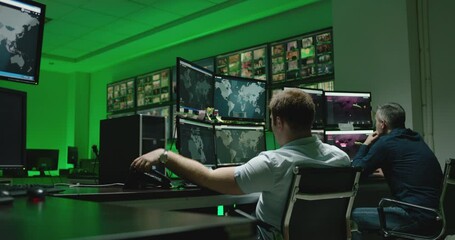Male workers sitting near computers on monitoring room and working . Programmers or engineers using many laptops , computers , searching , following information and statistics . Cyber security office 