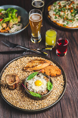 Close up of beef tartare served with two glasses of beer, one big potato pancake and baked zucchini.