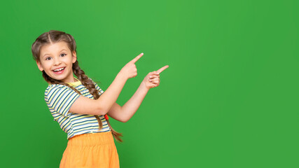 Wall Mural - A little girl points with both hands at the advertisement. Copy space. Isolated background.