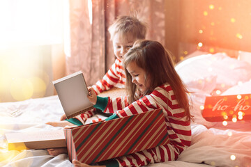 Canvas Print - Children in striped pajamas unpack Christmas gifts while sitting on white bed