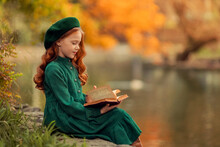 Beautiful Red-haired Girl In A Green Dress And Take A Walk In The Autumn In The Park With A Book In Her Hands