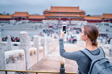 Wall Mural - Enjoying vacation in China. Travel and technology. Young woman with smartphone taking photo at Forbidden City, Beijing.
