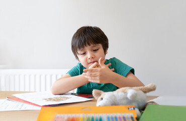Portrait of school kid sitting alone doing homework, Child boy holding brown pen drawing and writing on white paper on table, Elementary school and homeschooling concept
