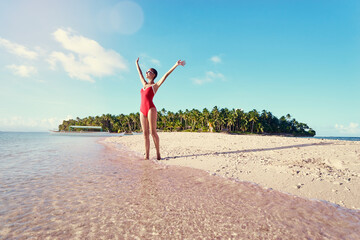 Wall Mural - Vacation and freedom. Happy young woman rising hands up standing on tropical beach enjoying beautiful view.