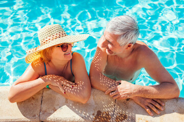 Wall Mural - Senior couple relaxing in swimming pool. People enjoying summer vacation in hotel. All inclusive.