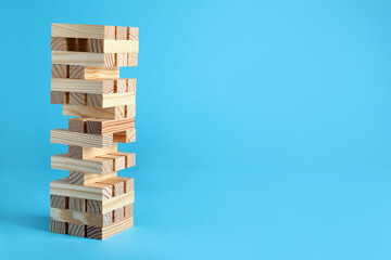 Wall Mural - Jenga tower made of wooden blocks on light blue background, space for text