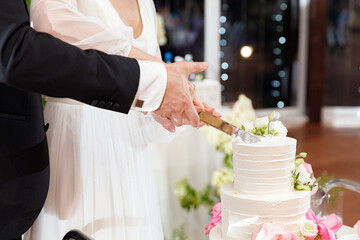 Wall Mural - Bride and groom holding knife and cutting stylish white wedding cake with flowers. modern big wedding cake with pink and white roses