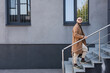 full length view of trendy asian man walking upstairs near grey building