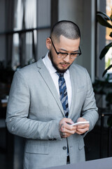 Sticker - asian businessman in formal wear and eyeglasses messaging on cellphone in office