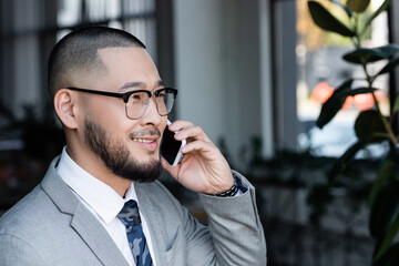 Wall Mural -  asian businessman in eyeglasses talking on mobile phone and smiling in office