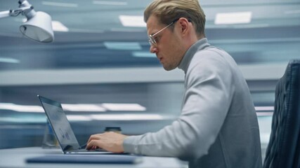 Poster - Modern Office: Handsome Businessman Sitting at His Desk Working on a Laptop Computer. Man working with Big Data e-Commerce Analysis. Energetic 360 Degree Fast Tracking Shot. Camera Moving Around