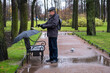 Adult man in jacket and cap puts on gloves in cold rainy weather in park while walking. Autumn, it's raining. Selective focus.