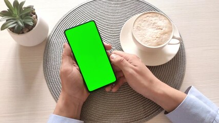 Man holding smartphone with vertical green screen and drinking coffee. Scrolling Through Social Media. Business concept. Mobile Phone with Chroma Key. Close up hands.