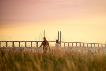 A couple looks out over the Öresund strait with the Öresund Bridge between Sweden and Denmark during sunset in Limhamn, Malmö.