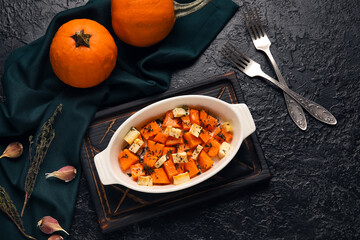 Baking dish with tasty roasted pumpkin on black background