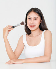 Wall Mural - Portrait beauty studio shot of millennial Asian short black hair female model in tank top vest undershirt place arm on table holding concealer brush in hand look at camera on white background