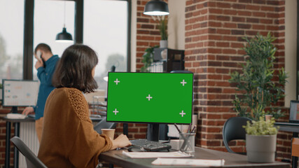 Wall Mural - Employee looking at horizontal green screen on computer display at desk. Woman using monitor with isolated mockup template and chroma key to plan business project. Entrepreneur at work