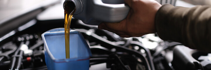 Wall Mural - Master repairman pouring motor oil into car engine closeup