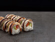 Japanese sushi roll with salmon, avocado and cream cheese inside roll. Asian dish pieces with eel on top served with sauce, dark concrete background. Copy space image. Single object. Inside out sushi
