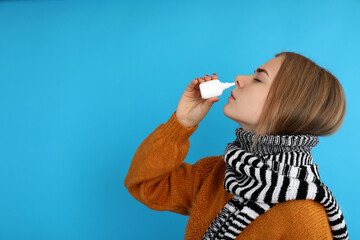 Young woman with nasal drops on blue background, runny nose concept