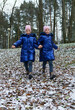 Two twin girls runing down hill covered with first snow