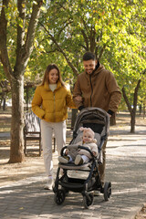 Poster - Happy parents walking with their baby in stroller at park on sunny day