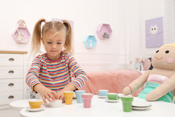 Sticker - Cute little girl playing tea party with doll at table in room