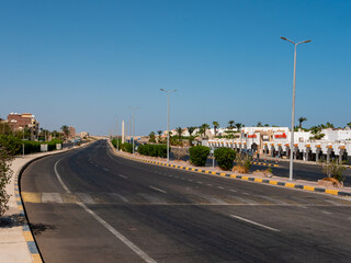 Safaga, Egypt - September 27, 2021: View of the main road stretching into the distance against the backdrop of the blue sky. Hotels, houses of local residents and shops were built near the road.